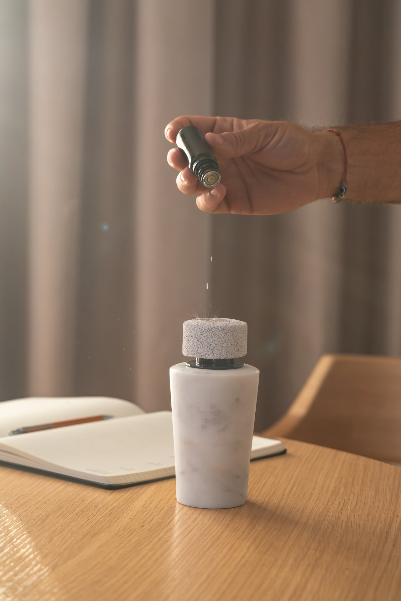 Oil dropping from a small bottle onto the pumice cap of a white marble diffuser