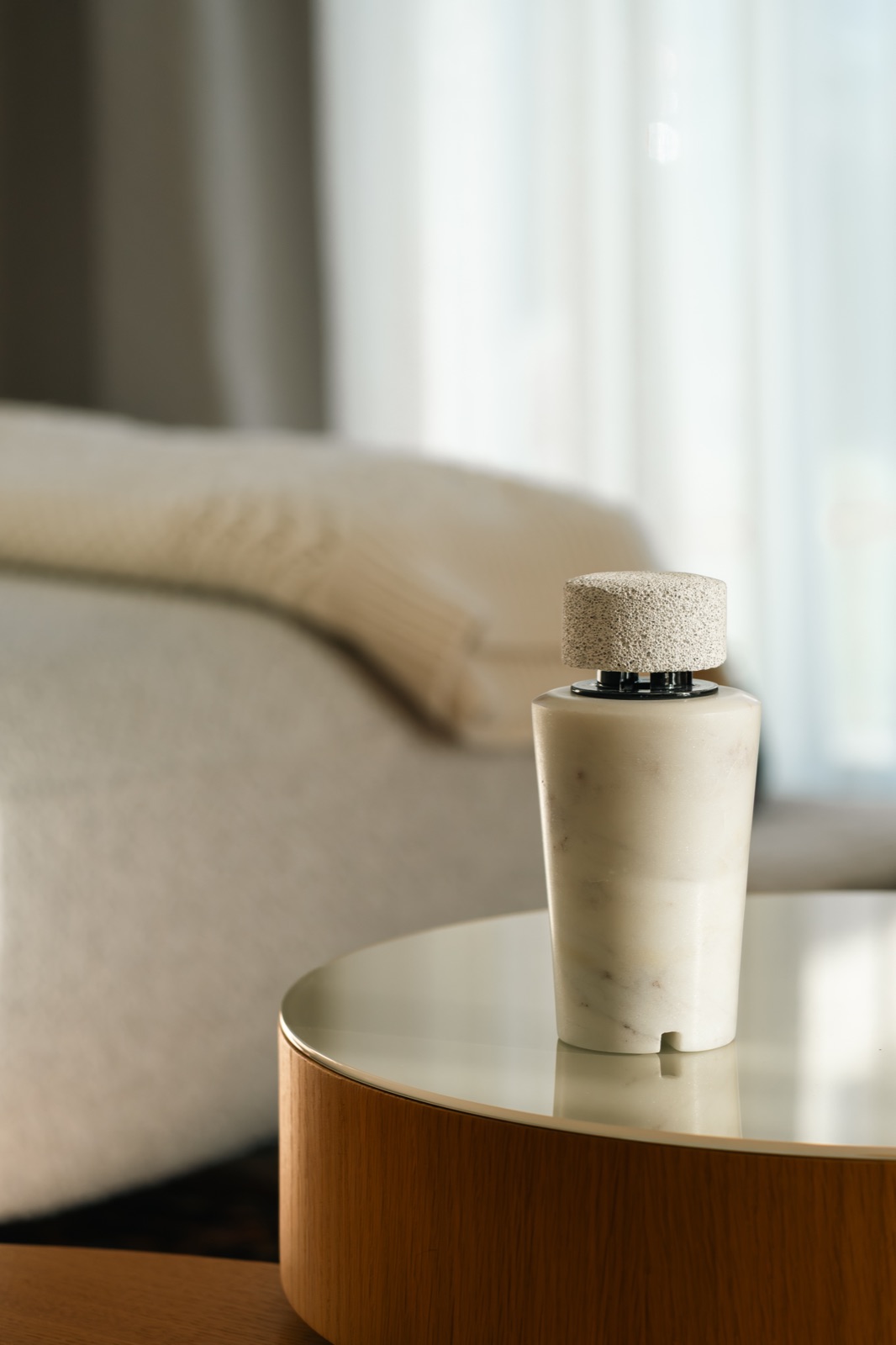 A white marble diffuser with a pumice cap on a round wooden side table by a sofa