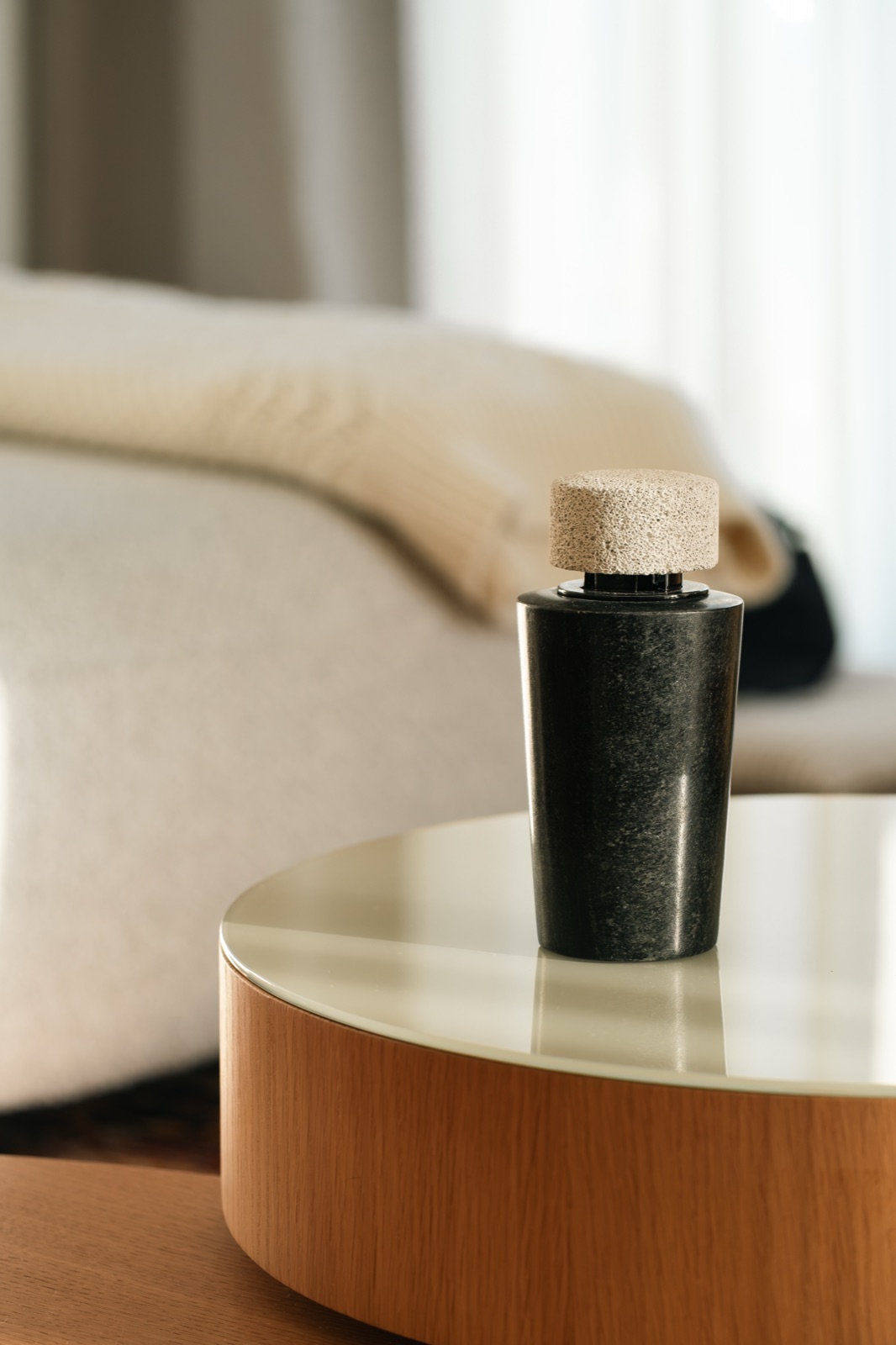 A black marble diffuser with a pumice cap on a round wooden side table by a sofa
