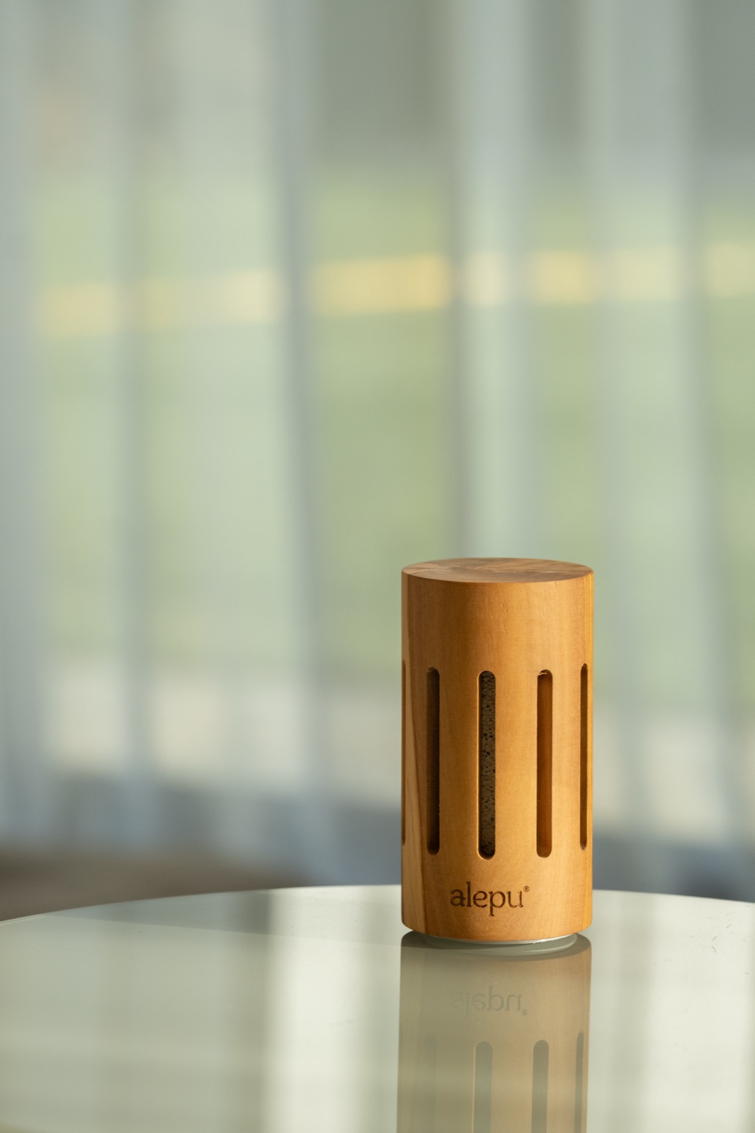 A round olive wood diffuser on a marble table in soft window light