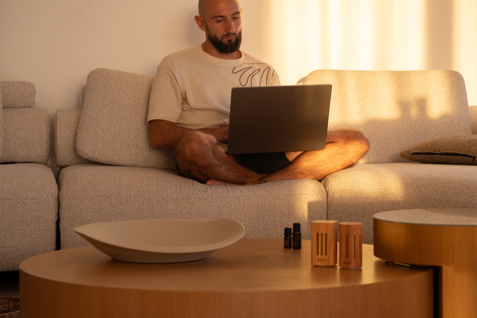 Olive wood diffusers on a low table in front of a sofa, a man working on a laptop behind