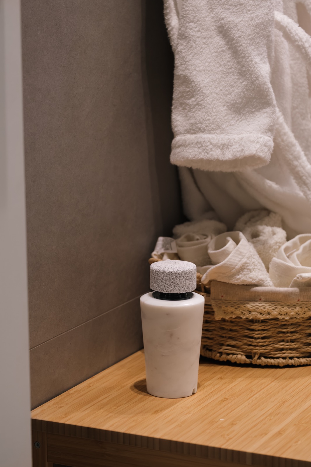 A white marble diffuser on a bathroom shelf beside rolled towels