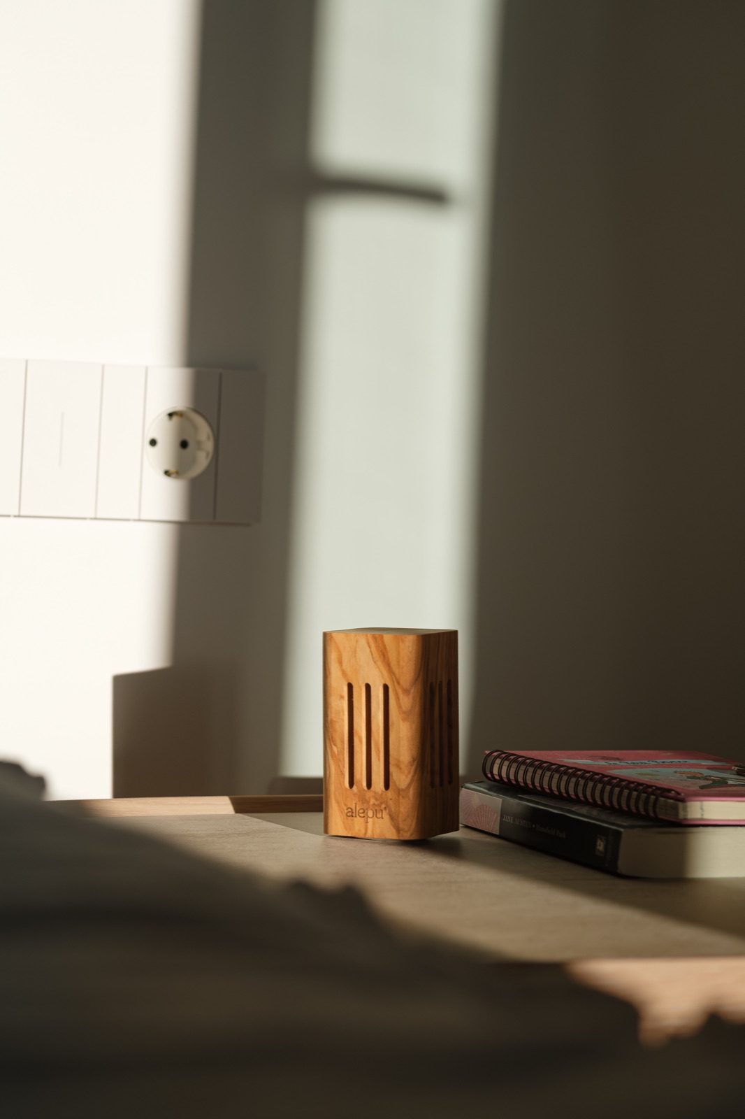 An olive wood diffuser on a hotel bedside table beside a stack of books