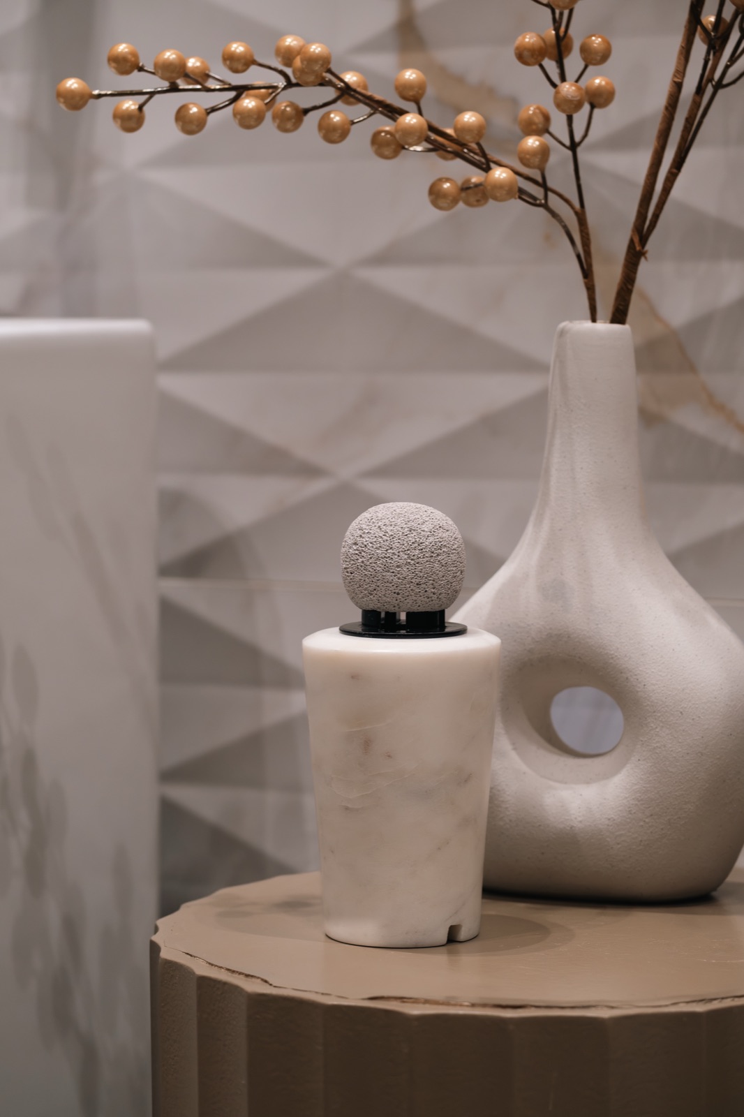 A white marble diffuser on a display stand beside a sculptural vase