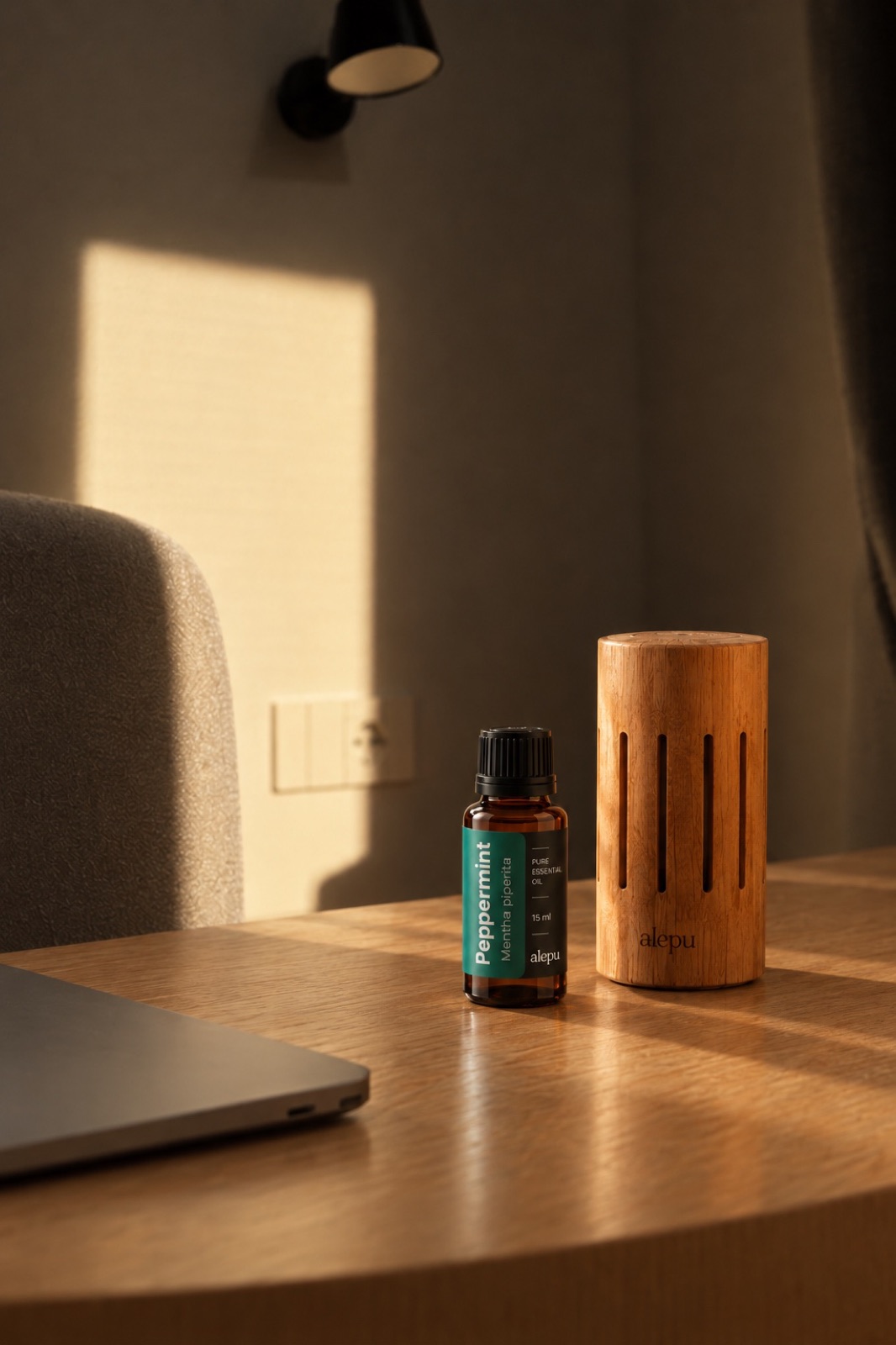 A bottle of Alepu peppermint essential oil beside an olive wood diffuser on a desk by a laptop