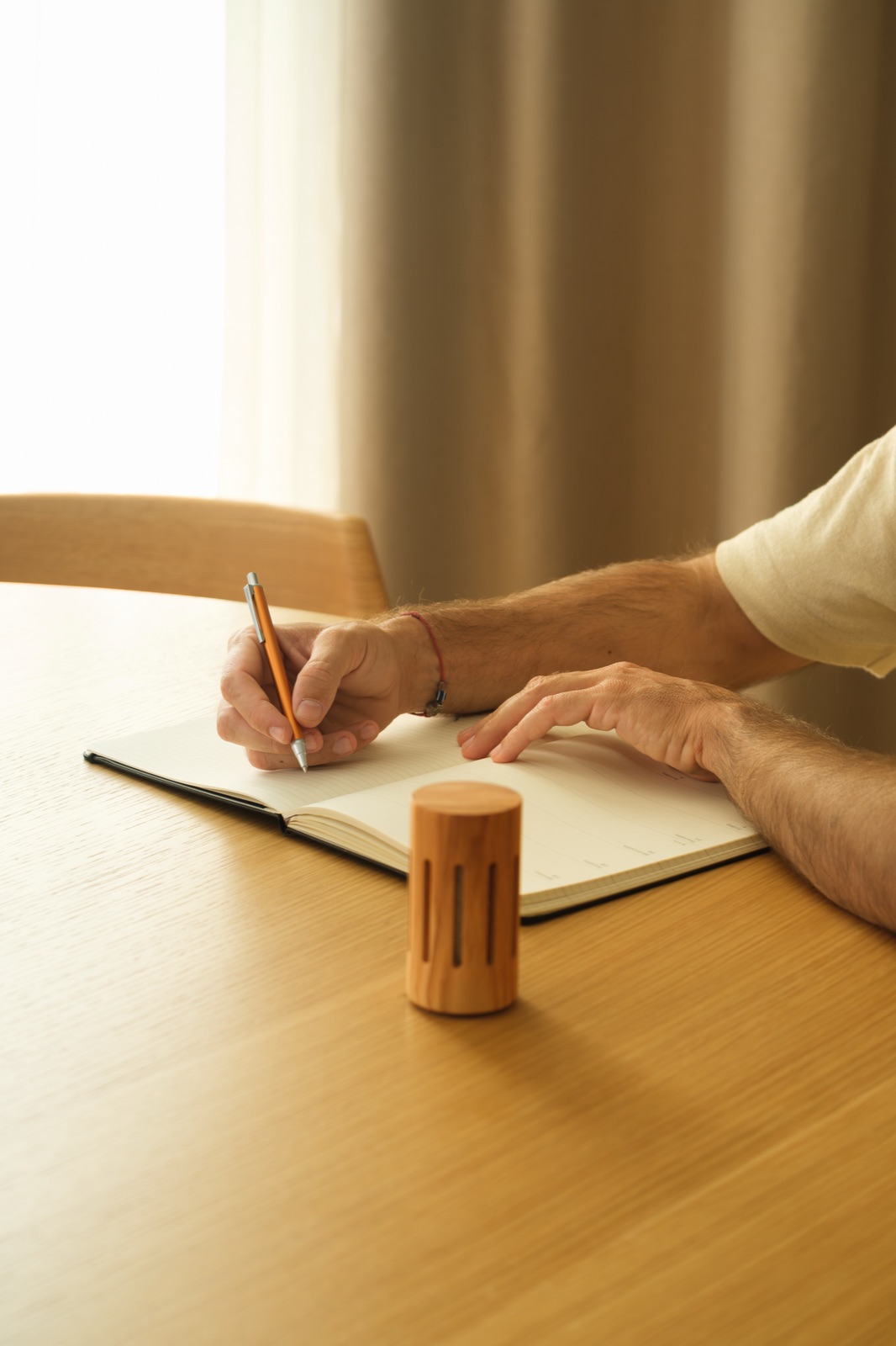 A round olive wood diffuser beside someone writing in a notebook