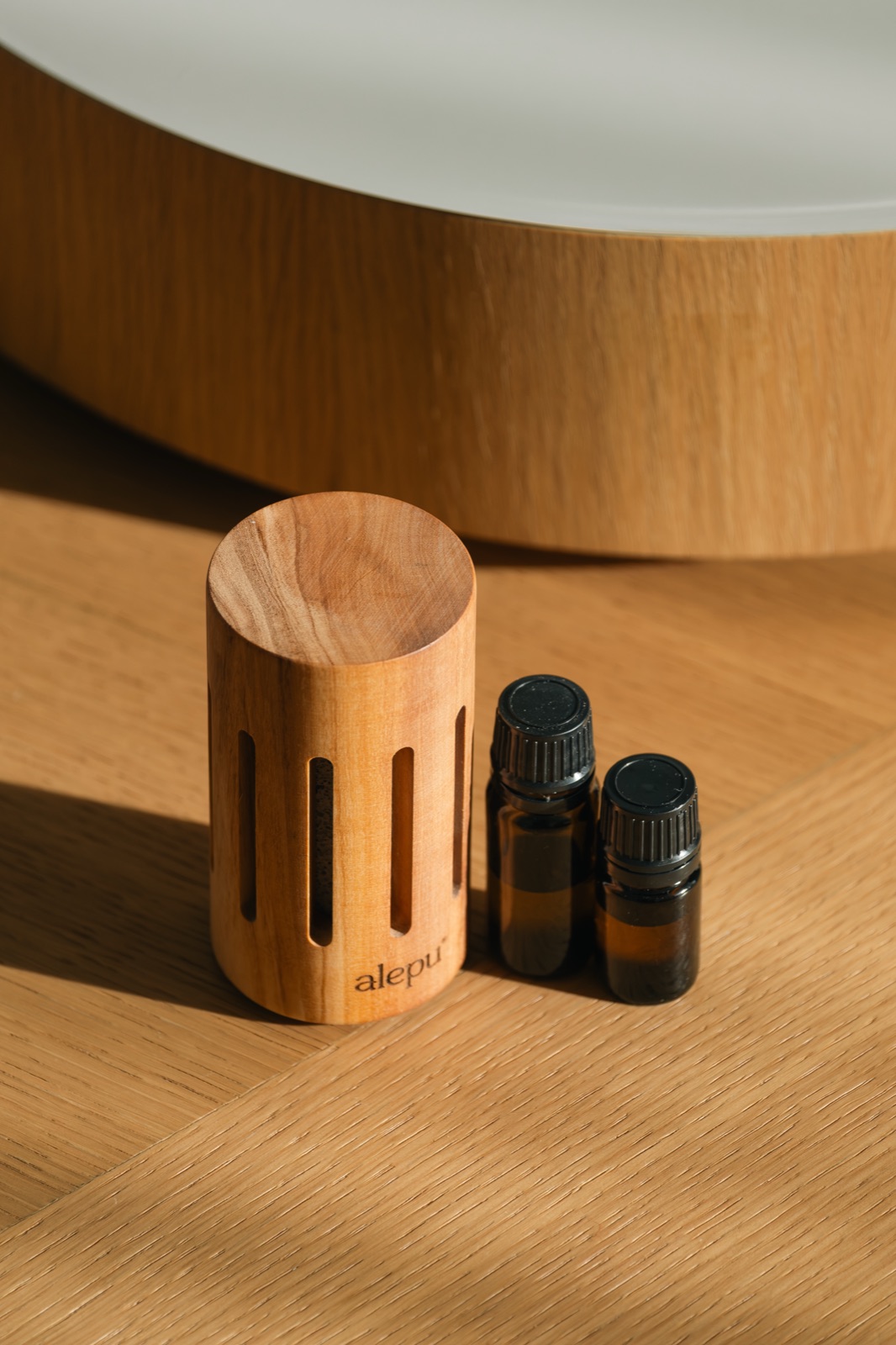 A round olive wood diffuser beside two bottles of essential oil