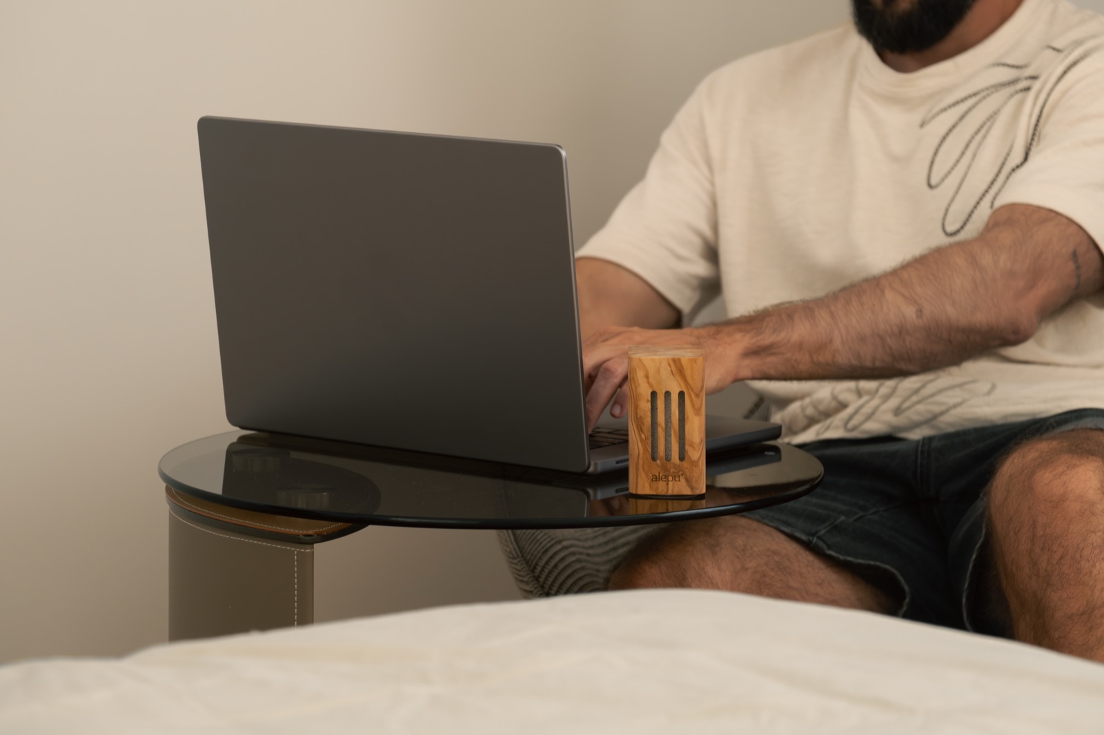 A man working on a laptop in bed beside an olive wood diffuser